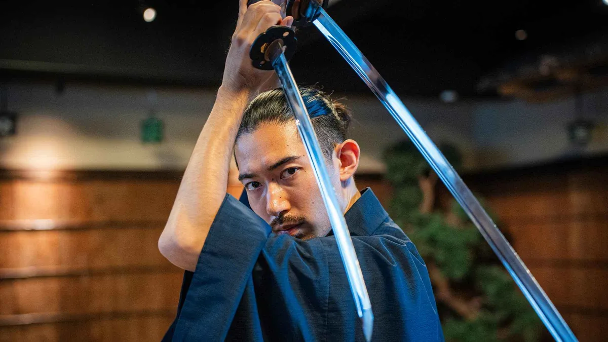 Visitor in hakama practicing a katana cut during a sword lesson at a samurai museum in Tokyo
